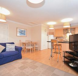 An open-plan living area with a blue sofa a dining table with chairs and a kitchen with a breakfast bar and stools at Beachcomber Apartment in Bamburgh