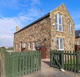 A stone house with a green fence and gate at Pipistrelle in Bamburgh
