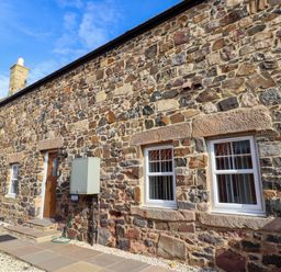 An exterior view of a stone building with windows and a wooden door at Pipistrelle in Bamburgh