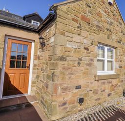 An outdoor area with a stone wall and door at Goosander in Bamburgh