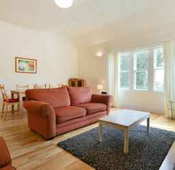 A living room with orange sofas a wooden coffee table a dining table with chairs a television and a large window at Decked Out in Alnmouth