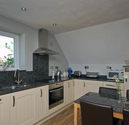 A kitchen with cream cabinets black countertops a window a stove a microwave and a table with chairs at Quarry Mews in Bamburgh