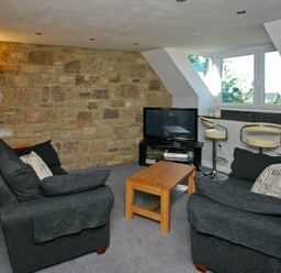 A living room with two sofas a wooden coffee table a television and two bar stools at Quarry Mews in Bamburgh