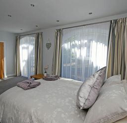 A bedroom with a bed pillows towels on it large windows with curtains and a wooden door at Quarry Mews in Bamburgh