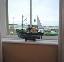 A model fishing boat on a windowsill with a view of cars and houses outside at Coastal Haven in Seahouses