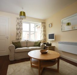 A living room with a sofa green cushions round wooden coffee table and wall-mounted heater at House Martins Beadnell