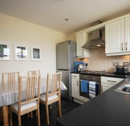 A kitchen with a dining table and chairs next to a fridge oven and sink at House Martins Beadnell