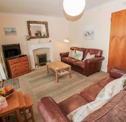 A living room with two brown leather sofas a wooden coffee table television on a wooden cabinet and a fireplace at Arcadie in Amble