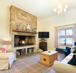 A living room with a stone fireplace a TV on the wall sofas and armchairs around a wooden chest at Charlton Cottage in Bamburgh