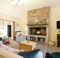 A living room with a stone fireplace a television mounted on the wall and upholstered chairs at Charlton Cottage in Bamburgh