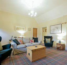 A living room with chairs sofa and wooden trunk table at Charlton Cottage in Bamburgh