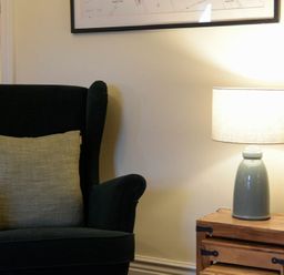 A black armchair with a beige cushion next to a wooden side table with a gray lamp on it at Charlton Cottage in Bamburgh
