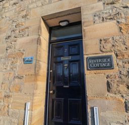 A black door with number 2 and a sign that says Riverside Cottage on a stone wall at Riverside Cottage in Warkworth