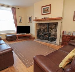 A living room with two leather sofas a fireplace and a television at Riverside Cottage in Warkworth
