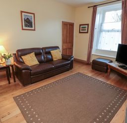 A living room with brown leather sofas a wooden coffee table a television a window with curtains and a lamp on a side table at Riverside Cottage in Warkworth
