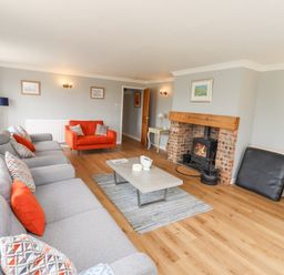 A living room with a gray sofa and orange armchair a coffee table on a rug and a fireplace at Jara in Bamburgh