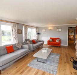 A living room with grey and red sofas a coffee table a fireplace and large windows at Jara in Bamburgh