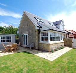 A stone house with patio furniture and shed in a garden at Stone Cottage Bamburgh