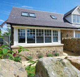 A stone house with large windows and a gated stone wall at Stone Cottage in Bamburgh