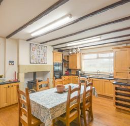 A kitchen with wooden cabinets a dining table with chairs and a window at Creel Cottage Amble