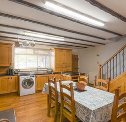 A kitchen with wooden cabinets a dining table with six chairs and kitchen appliances at Creel Cottage Amble