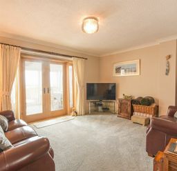 A living room with leather sofas TV and wooden doors with curtains at Creel Cottage Amble