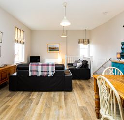 A living room with black sofas wooden dining table with chairs and blue cabinet at Baysyde in Alnmouth