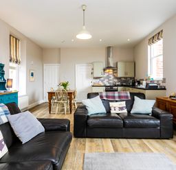 An open living room and kitchen with black leather sofas wooden dining table and blue cabinet at Baysyde in Alnmouth