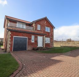 A two-story brick house with a garage and a driveway surrounded by grass and stone walls at Rathowen in Beadnell