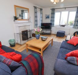 A living room with a wooden coffee table between two blue sofas and a television near the windows at Rathowen in Beadnell