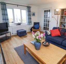 A living room with a blue sofa red cushions coffee table flowers books and a television at Rathowen in Beadnell