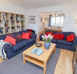 A living room with blue sofas and red cushions a wooden coffee table and a bookshelf at Rathowen in Beadnell