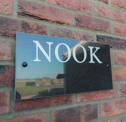 A black rectangular sign with the word NOOK on a red brick wall at Nook Cottage in Embleton