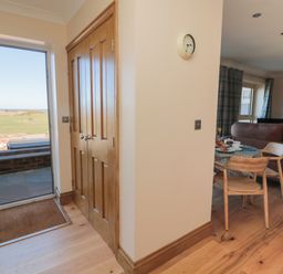 An entryway with wooden double doors and a doormat next to a dining area with a table, chairs, and brown sofas at Nook Cottage in Embleton