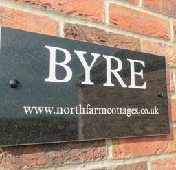 A black rectangular sign with the word BYRE and a website address mounted on a brick wall