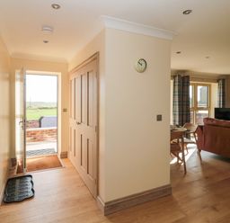 A hallway with wooden floor and doors leading outside and to a living room at Byre Cottage in Embleton