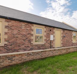 Exterior of a brick house with three windows a door and a low brick wall in front at Smithy Cottage in Embleton