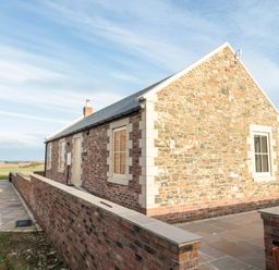 Exterior view of a stone and brick cottage with paved walkway and low brick wall at Bothy Cottage in Embleton