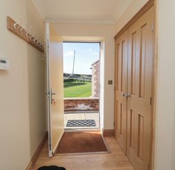 An entryway with an open door showing a green lawn outside a wooden closet and coat hooks on the wall at Bothy Cottage in Embleton