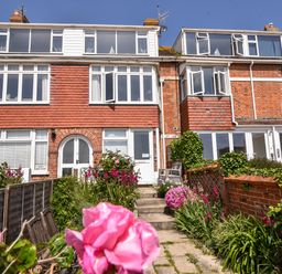 A two-story brick house with white framed windows and a garden path with flowers leading to the front door at The Penthouse @ No 5 in Lyme Regis