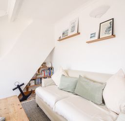 A living room with a beige sofa with cushions a wooden coffee table and wall shelves with pictures at The Penthouse @ No 5 in Lyme Regis