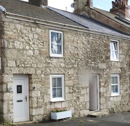 A stone cottage exterior with white framed windows and a white door with a flower box below at Pebble Reef in Easton Portland