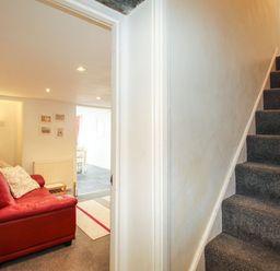 A hallway with a carpeted staircase and a room with a red sofa and lamp at Pebble Reef in Easton Portland