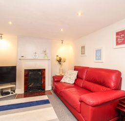 A living room with a red leather sofa a fireplace a television on a stand and framed pictures on the wall at Pebble Reef in Easton Portland