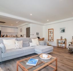 A living room with a gray sectional sofa and a wooden glass coffee table in an open plan area at 33 Cliff Edge in Newquay
