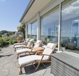 A patio with cushioned lounge chairs and a small table outside large glass windows at Raven Cottage in Downderry