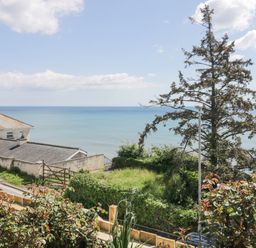 View of the sea with houses trees a street and plants in a garden at Raven Cottage in Downderry