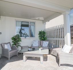 A covered patio with wicker chairs sofa a glass table and potted plants at Raven Cottage in Downderry