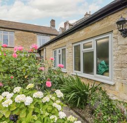 A garden with pink and white flowers next to a stone house with white windows and an outdoor lamp at 2 Church Street in Chipping Norton