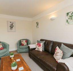 A living room with a brown leather sofa two green armchairs a wooden coffee table and wall art at 2 Church Street in Chipping Norton